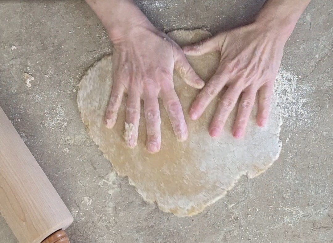 hands pressed onto einkorn noodle dough which has been rolled out